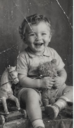Old photo of a toddler with a teddy bear, covered in deep scratches and creases